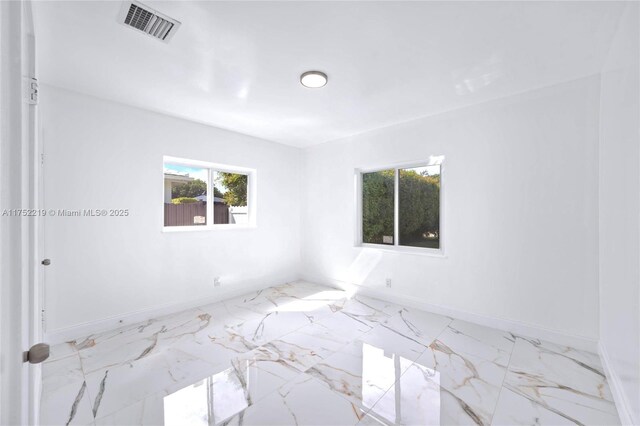 spare room with marble finish floor, visible vents, and baseboards