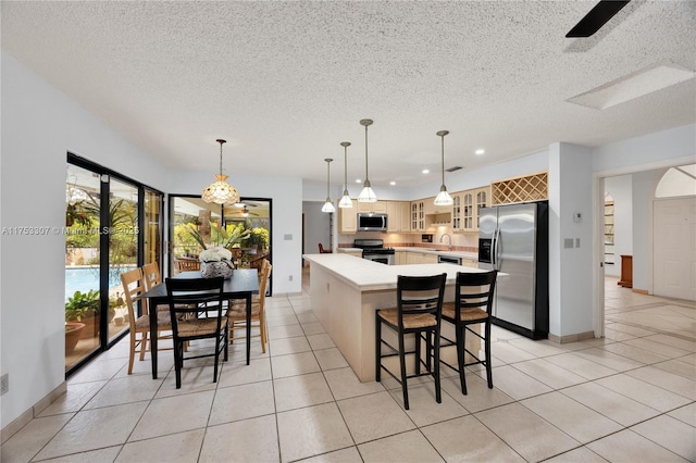 kitchen with stainless steel appliances, light countertops, glass insert cabinets, light tile patterned flooring, and a kitchen island