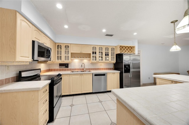 kitchen featuring tile counters, appliances with stainless steel finishes, a sink, and light brown cabinetry