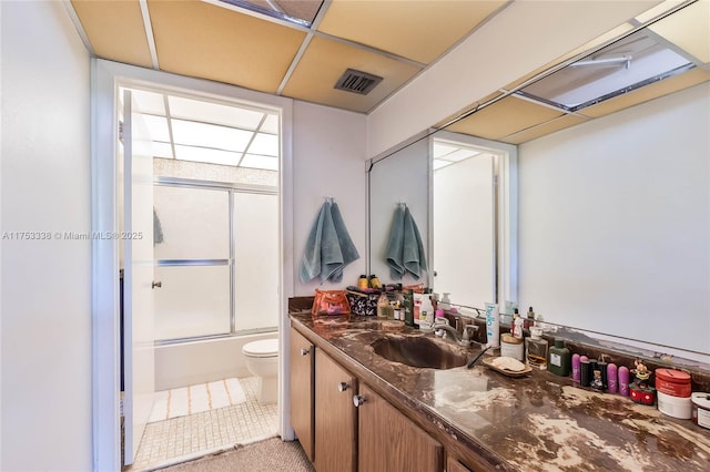 full bathroom with visible vents, toilet, combined bath / shower with glass door, vanity, and a paneled ceiling