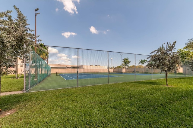 view of tennis court with a yard and fence