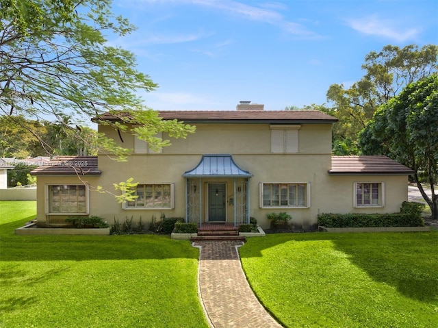 mediterranean / spanish home with a chimney, metal roof, a standing seam roof, a front lawn, and stucco siding