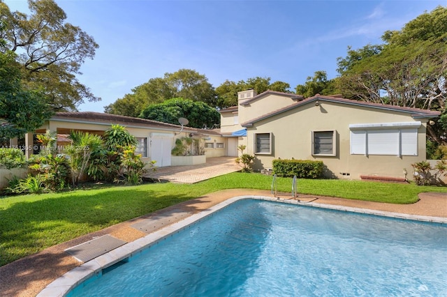 back of house featuring an outdoor pool, a yard, a patio, and stucco siding