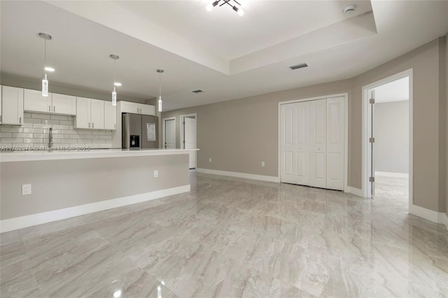 unfurnished living room featuring a raised ceiling, visible vents, and baseboards