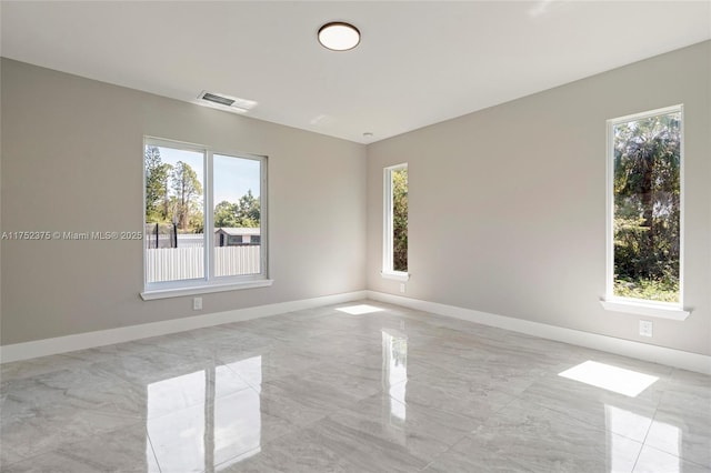 empty room with marble finish floor, plenty of natural light, visible vents, and baseboards