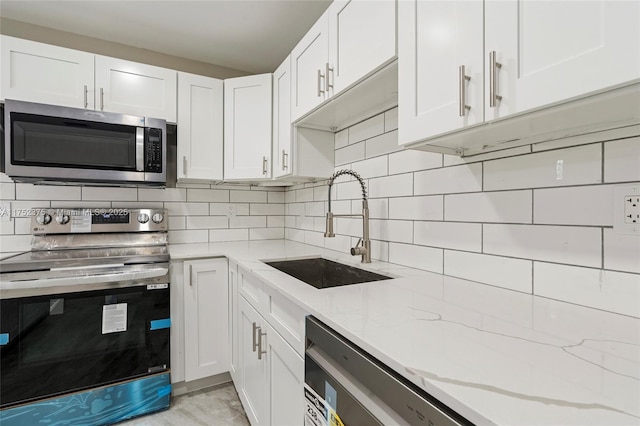 kitchen featuring decorative backsplash, light stone counters, appliances with stainless steel finishes, white cabinetry, and a sink