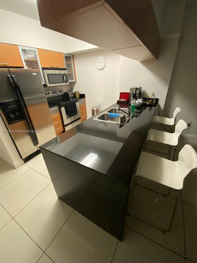 interior space with stainless steel appliances, dark countertops, glass insert cabinets, light tile patterned flooring, and a sink