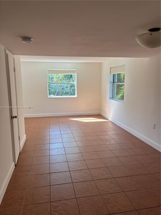 unfurnished room with dark tile patterned floors, plenty of natural light, and baseboards