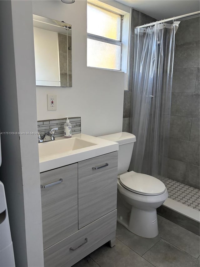 bathroom with tiled shower, tile patterned flooring, vanity, and toilet