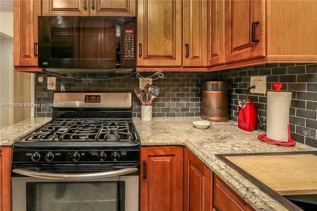 kitchen with light stone counters, brown cabinets, backsplash, stainless steel range with gas stovetop, and black microwave