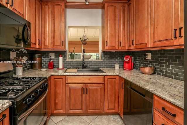 kitchen with light stone counters, stainless steel range with gas cooktop, backsplash, a sink, and black microwave