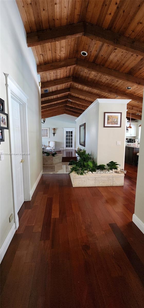 corridor with vaulted ceiling with beams, wooden ceiling, wood-type flooring, and baseboards