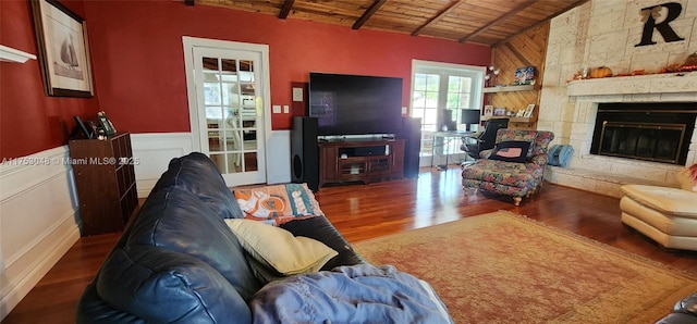 living room featuring lofted ceiling, a large fireplace, wainscoting, wood finished floors, and wooden ceiling