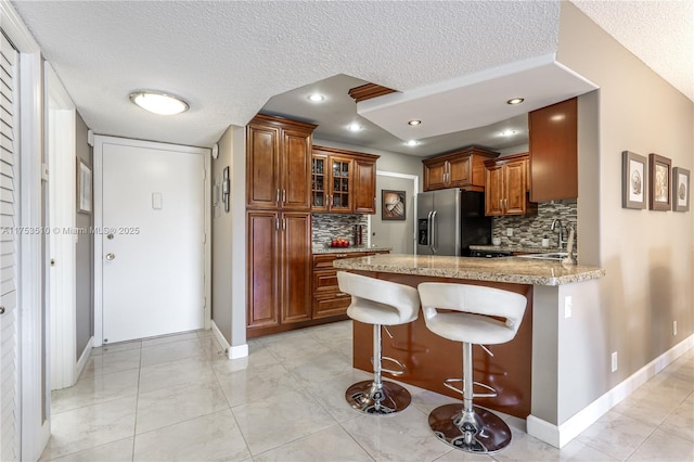 kitchen with a breakfast bar area, a peninsula, brown cabinetry, stainless steel fridge, and glass insert cabinets