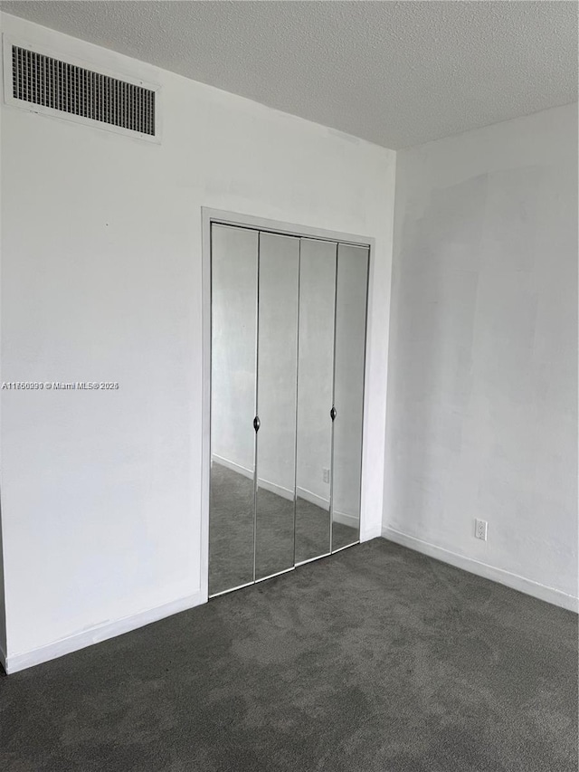 unfurnished bedroom featuring a textured ceiling, visible vents, baseboards, a closet, and dark colored carpet