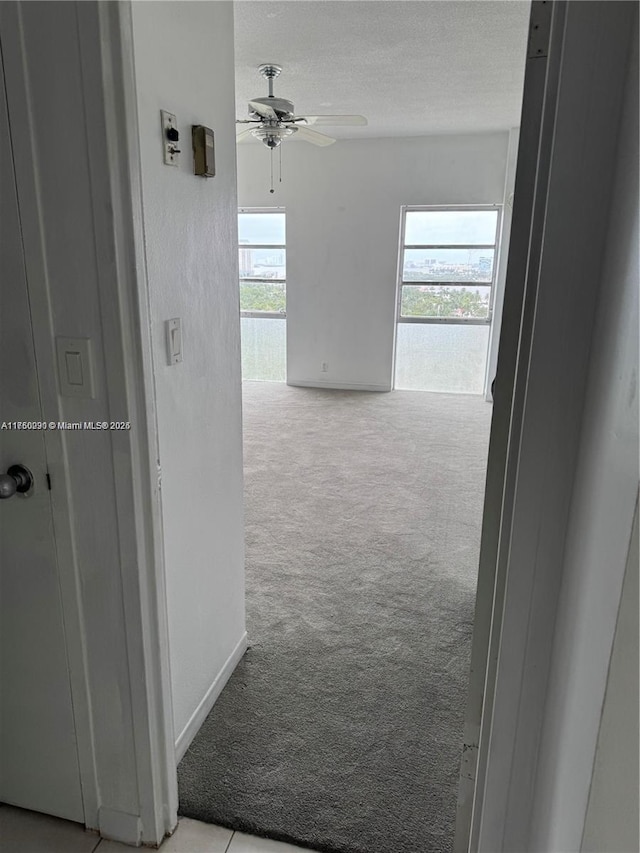 corridor featuring a textured ceiling, carpet floors, and baseboards