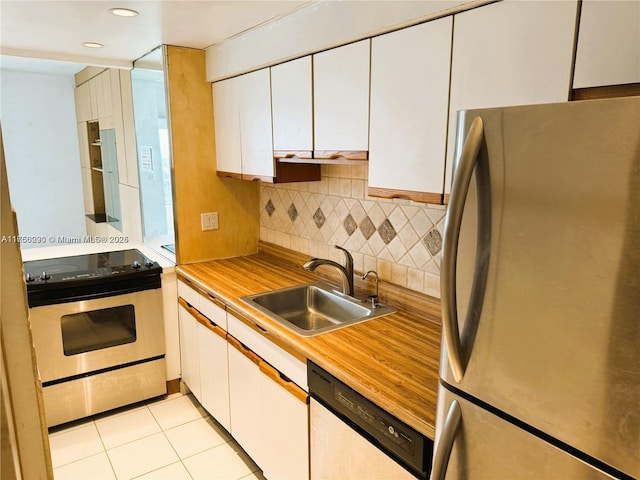 kitchen featuring light tile patterned floors, decorative backsplash, stainless steel appliances, white cabinetry, and a sink