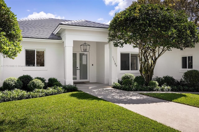 view of front of house with stucco siding, a tiled roof, a front yard, and french doors