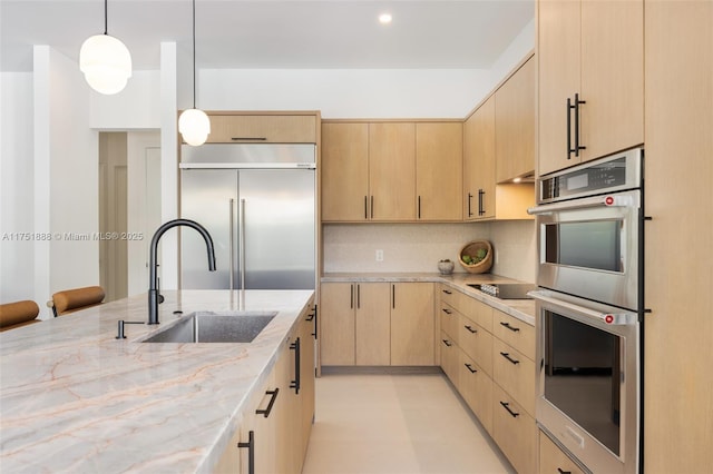 kitchen with appliances with stainless steel finishes, a sink, light stone countertops, light brown cabinetry, and backsplash