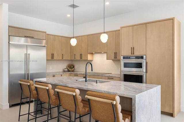 kitchen with tasteful backsplash, light brown cabinetry, appliances with stainless steel finishes, a sink, and light stone countertops