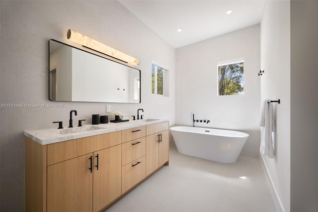 full bath featuring a freestanding bath, double vanity, a sink, and recessed lighting