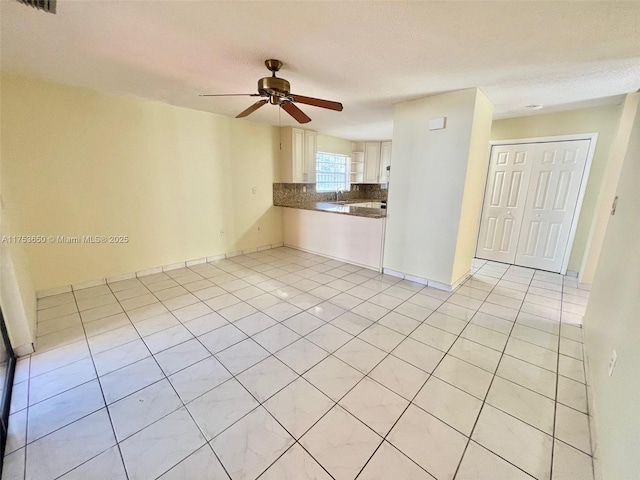 kitchen featuring decorative backsplash, a ceiling fan, white cabinets, a sink, and light tile patterned flooring