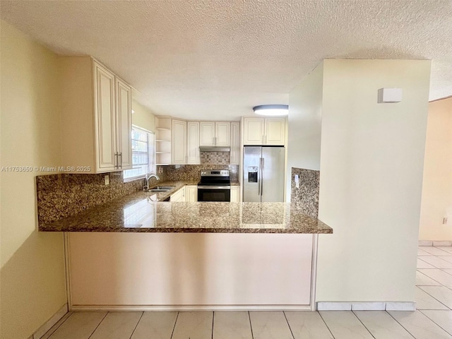 kitchen with stainless steel appliances, backsplash, a sink, dark stone countertops, and a peninsula