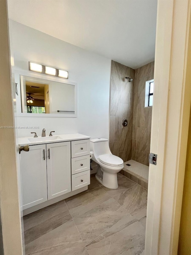 full bath featuring tiled shower, vanity, and toilet