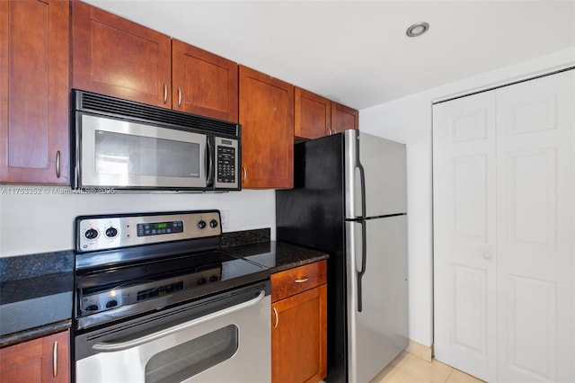 kitchen featuring light tile patterned floors, stainless steel appliances, brown cabinetry, and dark stone counters