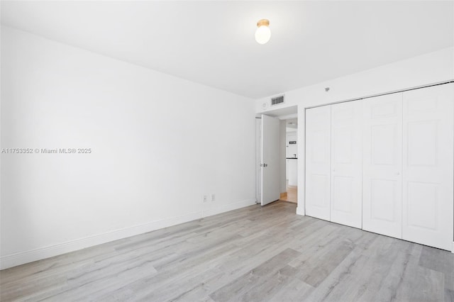 unfurnished bedroom featuring light wood-type flooring, a closet, visible vents, and baseboards