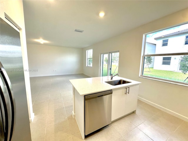 kitchen featuring baseboards, an island with sink, light countertops, stainless steel dishwasher, and a sink