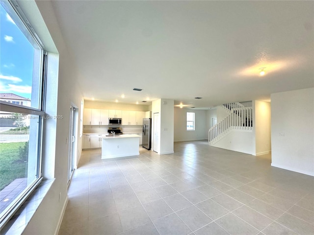 unfurnished living room with stairs, light tile patterned floors, visible vents, and baseboards