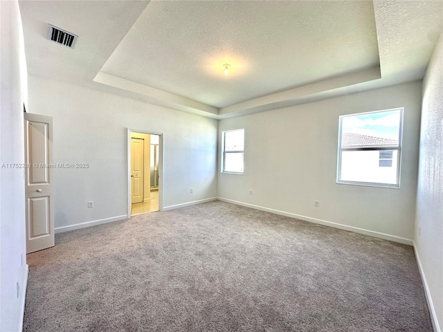 unfurnished bedroom with carpet floors, a tray ceiling, visible vents, a textured ceiling, and baseboards