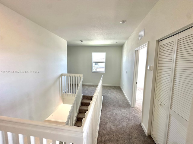 hall featuring baseboards, carpet flooring, a textured ceiling, and an upstairs landing