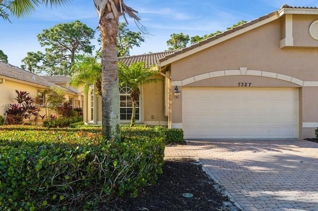 view of front of house featuring a garage, decorative driveway, a tile roof, and stucco siding