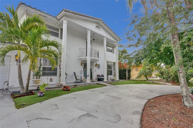 greek revival inspired property featuring a balcony, a tile roof, concrete driveway, and stucco siding