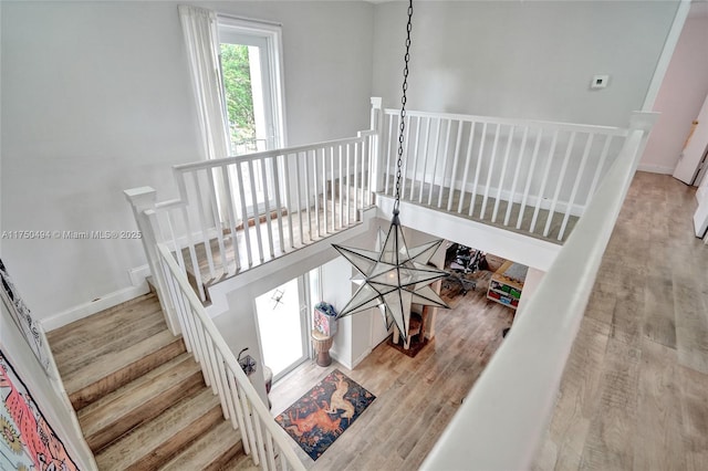 staircase featuring baseboards, wood finished floors, and an inviting chandelier