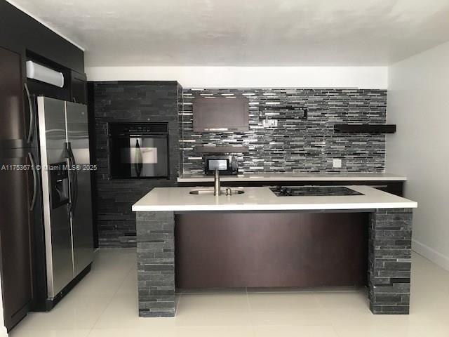 kitchen with a center island with sink, light countertops, light tile patterned flooring, modern cabinets, and black appliances