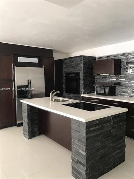 kitchen featuring black appliances, light countertops, a sink, and a center island with sink