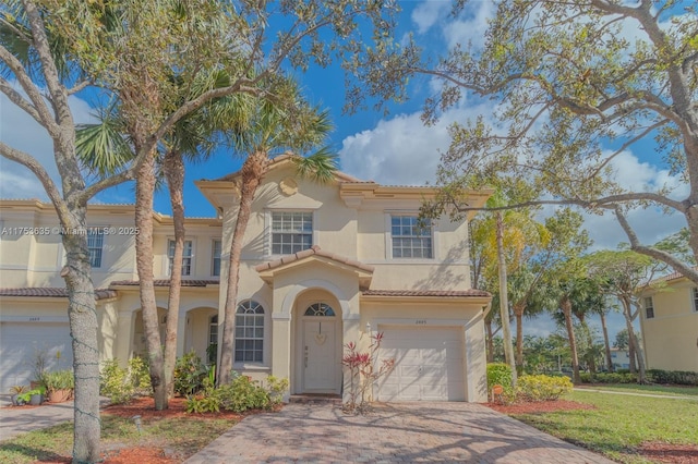 mediterranean / spanish-style home with a garage, decorative driveway, a tile roof, and stucco siding