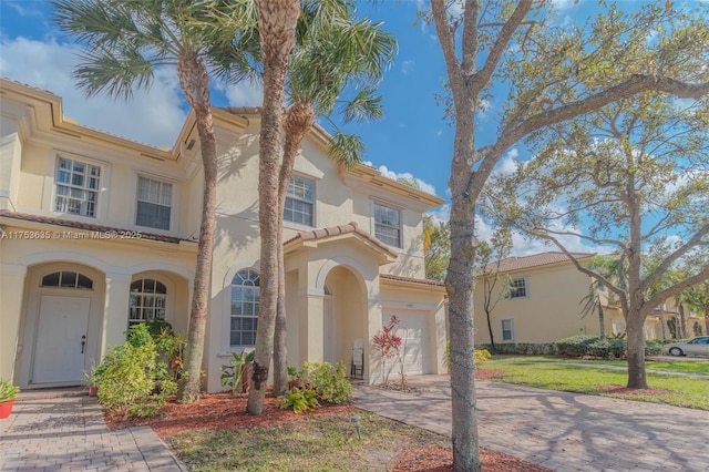 mediterranean / spanish house with an attached garage, decorative driveway, and stucco siding