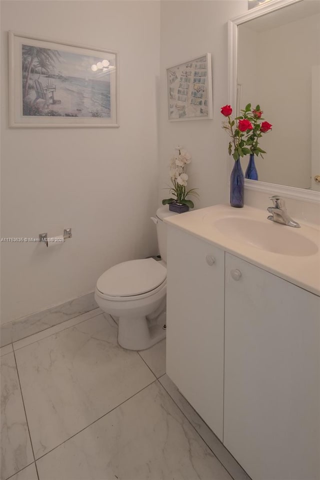 half bathroom with marble finish floor, baseboards, vanity, and toilet