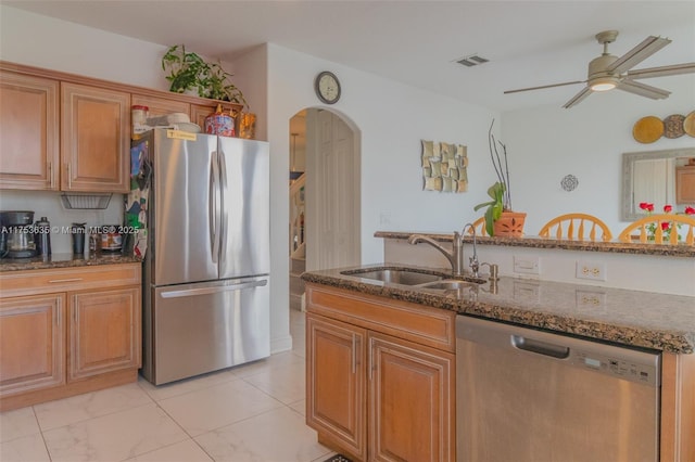 kitchen with arched walkways, appliances with stainless steel finishes, dark stone counters, and a sink