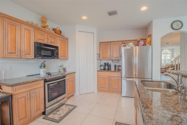 kitchen with arched walkways, stainless steel appliances, recessed lighting, a sink, and dark stone counters