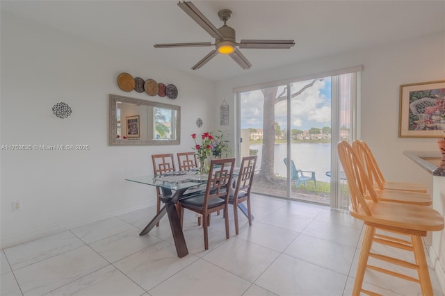 dining area featuring a water view, baseboards, and a ceiling fan