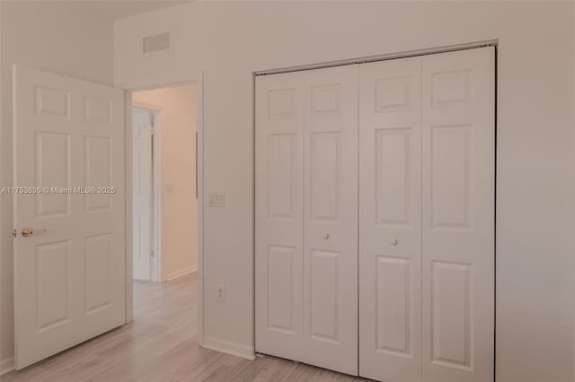 unfurnished bedroom with light wood-type flooring, a closet, visible vents, and baseboards