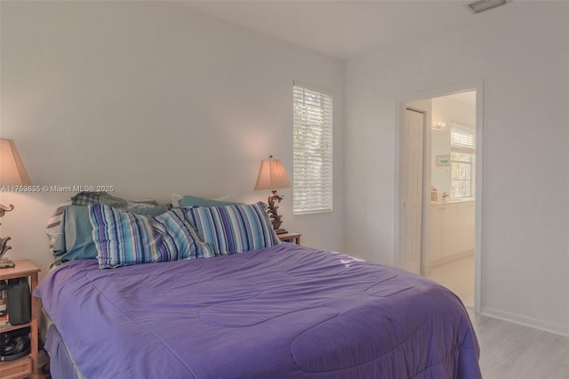 bedroom with ensuite bathroom, wood finished floors, and visible vents