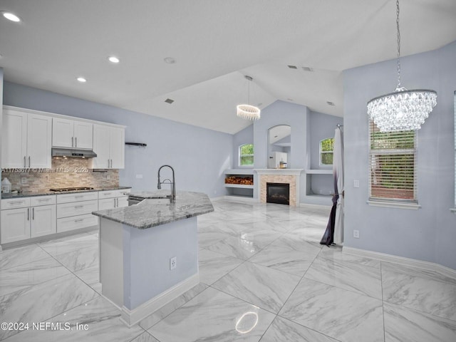 kitchen with light stone counters, white cabinets, a sink, and under cabinet range hood