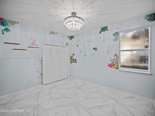 bedroom featuring a textured ceiling, a closet, a notable chandelier, and baseboards