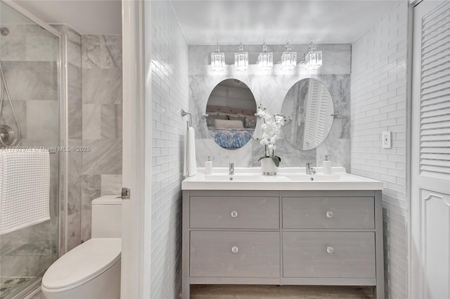 bathroom with tile walls, double vanity, toilet, a sink, and a shower stall